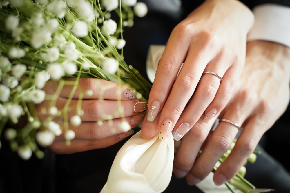 結婚指輪を着けたふたりの手元とかすみ草のブーケ