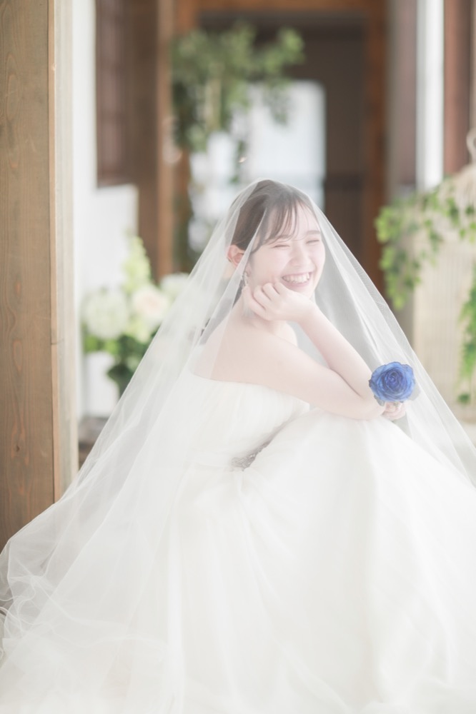 ベールをまとい笑顔でブルーローズを持つ花嫁